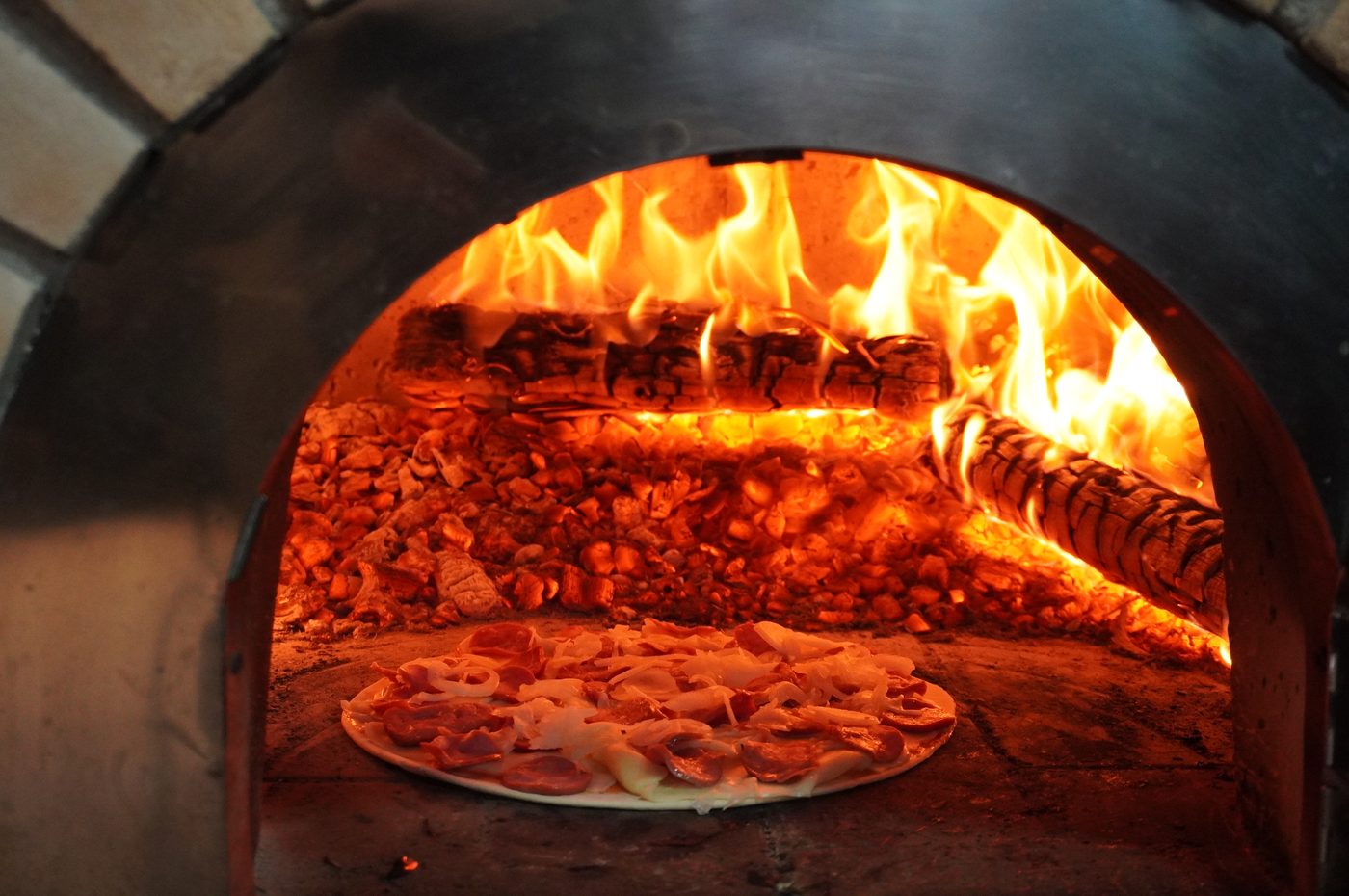Pizza assando em forno com chamas ao fundo durante o serviço